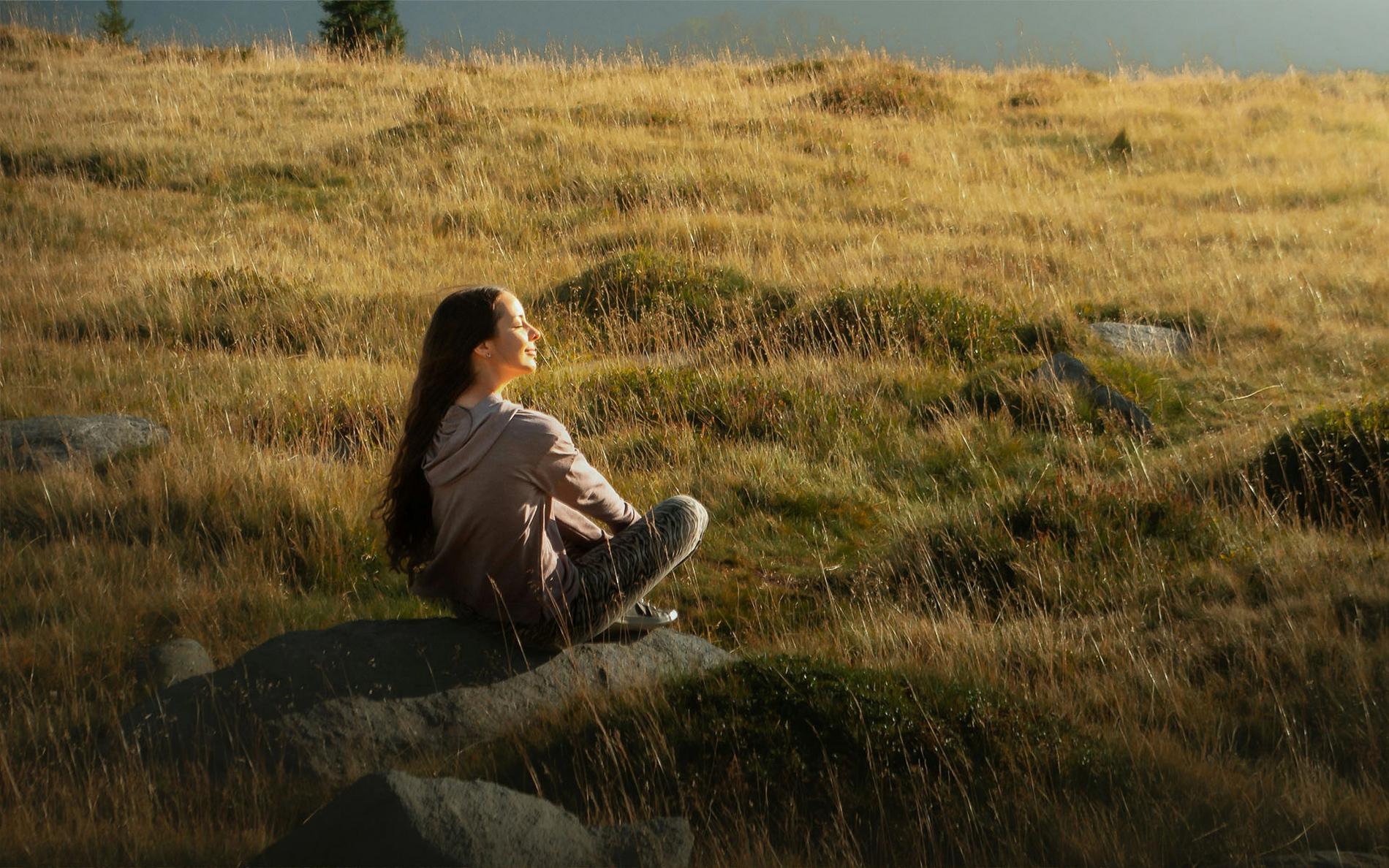 Frau sitzt ruhig in Natur auf Felsen im warmen Abendlicht