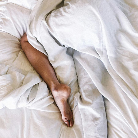 Bein ragt entspannt aus der Bettdecke im Hotelbett