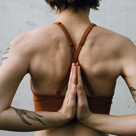 Frau in Yoga-Pose mit gefalteten Händen hinter dem Rücken