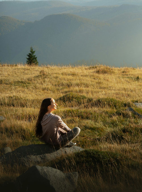 Frau sitzt entspannt auf einer Wiese mit Bergblick