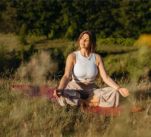 Frau meditiert auf einer Wiese in der Natur