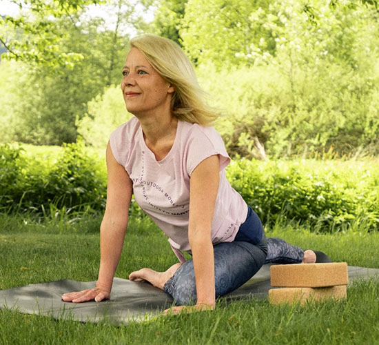 Frau macht Yoga auf einer Matte im Grünen
