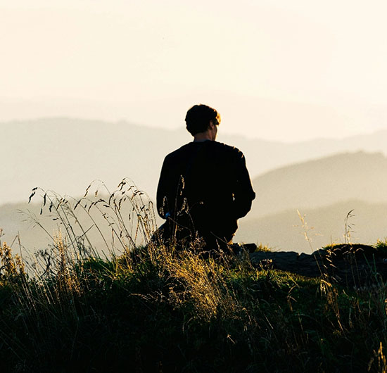 Person sitzt auf einem Berg im Sonnenuntergang