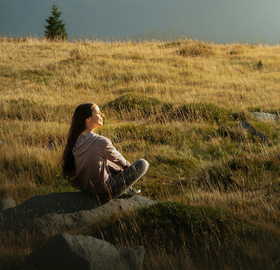 Frau sitzt auf einer Wiese mit Blick auf Berge