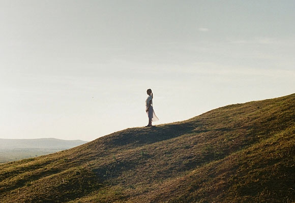 Frau steht auf einem Hügel und blickt über die Landschaft