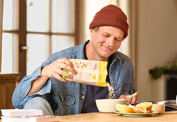 Mann bereitet Frühstück mit Müsli und frischen Zutaten zu