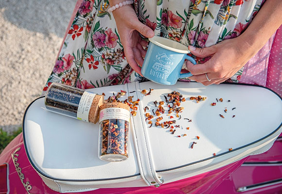 Frau bereitet Tee aus Kräutern und Blüten auf einem Tablett zu