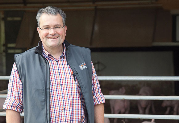Landwirt steht vor einem Stall mit Schweinen auf seinem Hof