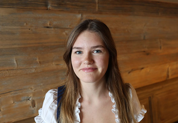 Junge Mitarbeiterin mit langen braunen Haaren vor Holzverkleidung