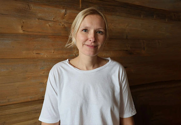 Mitarbeiterin mit blonden Haaren und weißem T-Shirt vor Holzwand