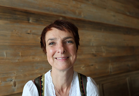 Mitarbeiterin mit kurzem Haar und Trachtenoberteil vor Holzpaneelen
