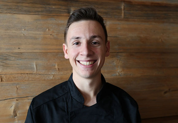 Junger Koch in schwarzer Kochjacke lächelt in die Kamera