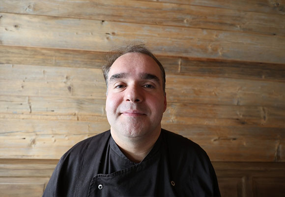 Koch mit schwarzer Kochjacke vor Holzverkleidung