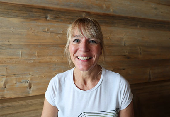 Blonde Mitarbeiterin mit weißem Shirt lächelt vor Holzwand