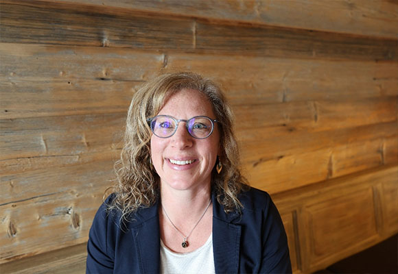 Mitarbeiterin mit Brille und lockigen Haaren vor Holzpaneelen