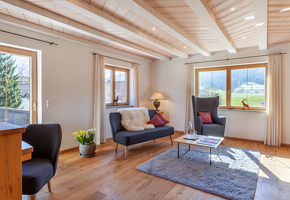 Helles Chaletzimmer mit Sofa, Sesseln und Blick ins Grüne