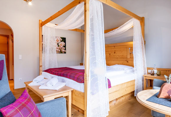 Doppelzimmer mit Himmelbett aus Holz und gemütlicher Sitzecke