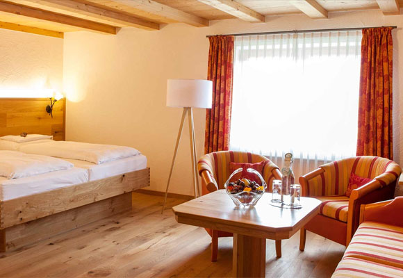 Doppelzimmer mit Sitzecke, Holzmöbeln und großem Fenster