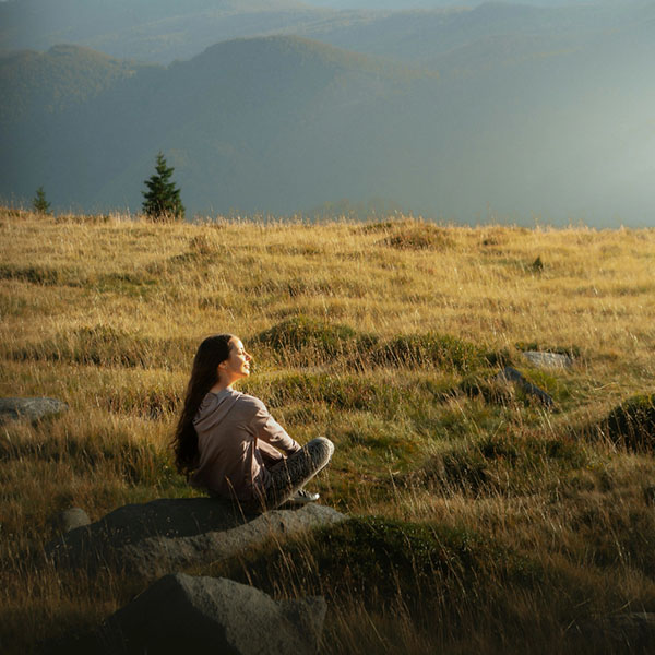 Frau sitzt entspannt auf einem Felsen in einer Bergwiese im Allgäu