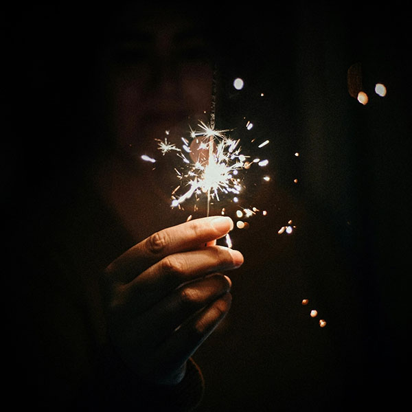 Hand hält eine brennende Wunderkerze im Dunkeln