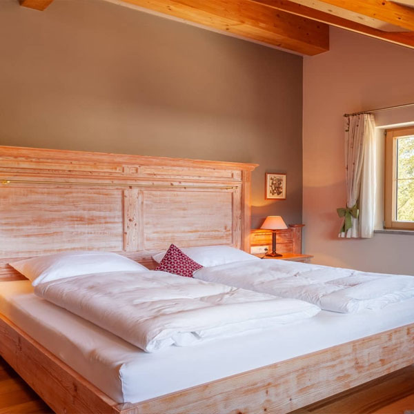 Detailaufnahme eines großen Holzbetts mit weißer Bettwäsche