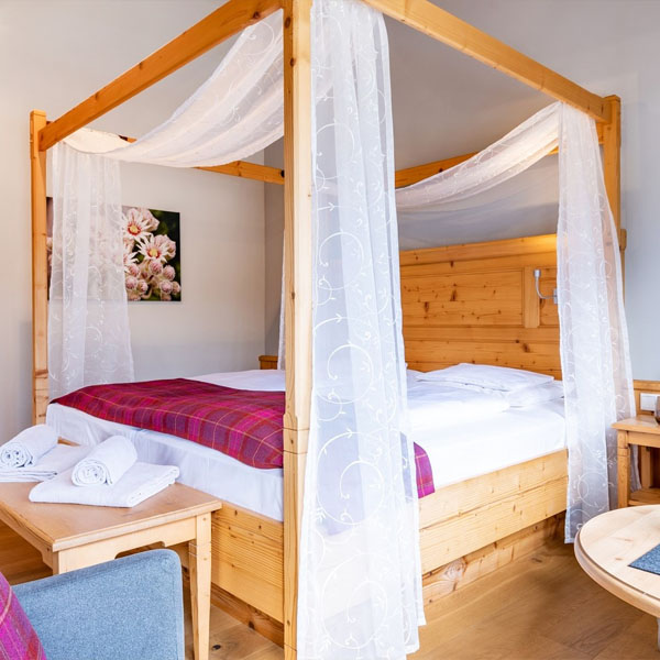 Doppelzimmer mit großem Holzbett und Sitzbereich am Fenster