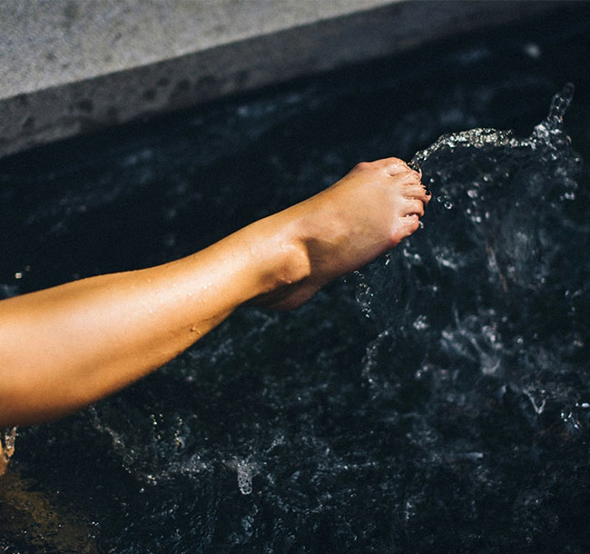 Fuß taucht in spritzendes Wasser eines Kneippbeckens