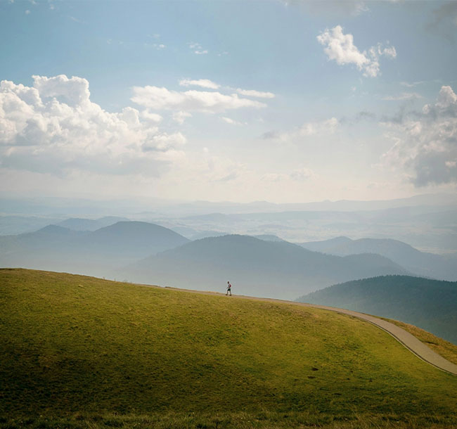 Person wandert auf einem Hügel mit weiter Berglandschaft im Hintergrund