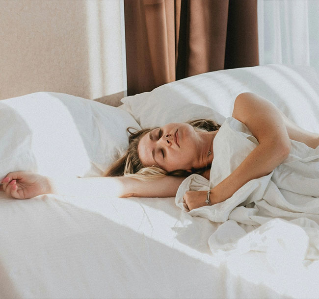 Frau schläft entspannt in einem hellen Hotelbett