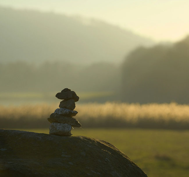 Kleine Steinpyramide auf einem Felsen vor ruhiger Landschaft