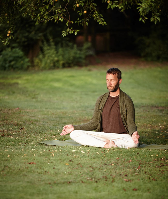 Mann meditiert im Schneidersitz auf einer Wiese im Park