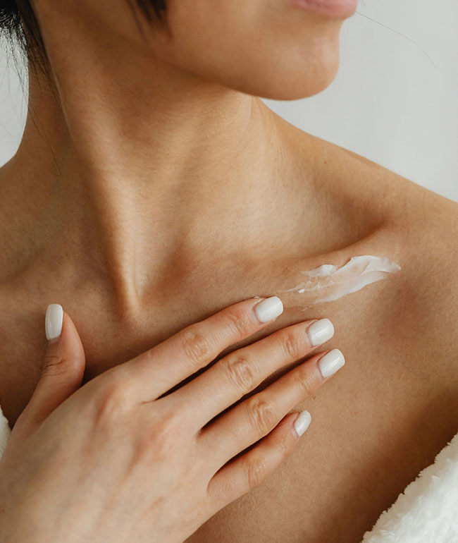 Frau trägt Pflegecreme auf Schulter und Dekolleté auf