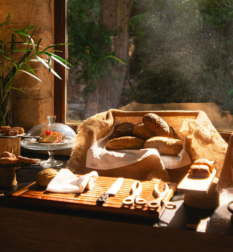 Brotkorb mit frischem Brot auf einem Holztisch im warmen Morgenlicht am Fenster