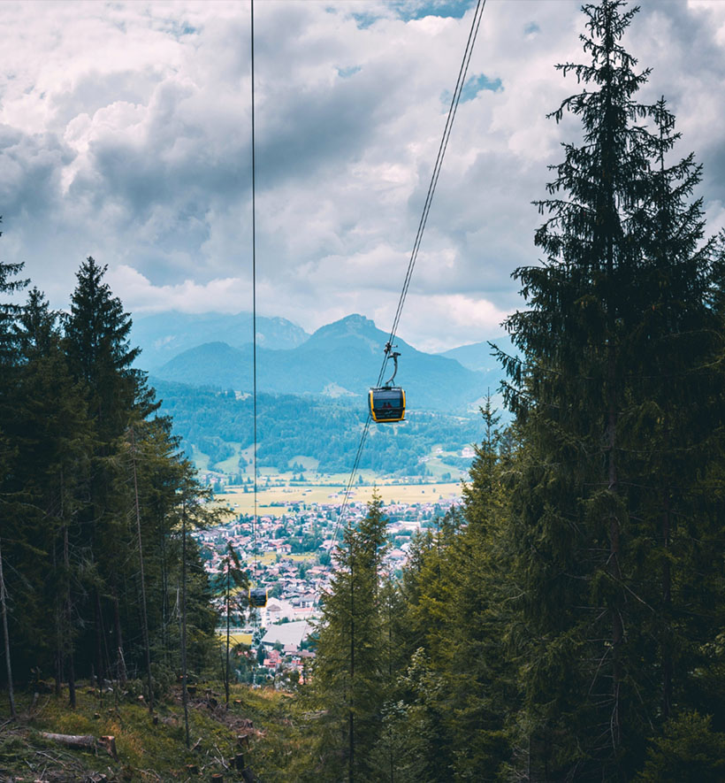 Seilbahn fährt über bewaldete Hänge mit Blick ins Allgäuer Tal und die Berge