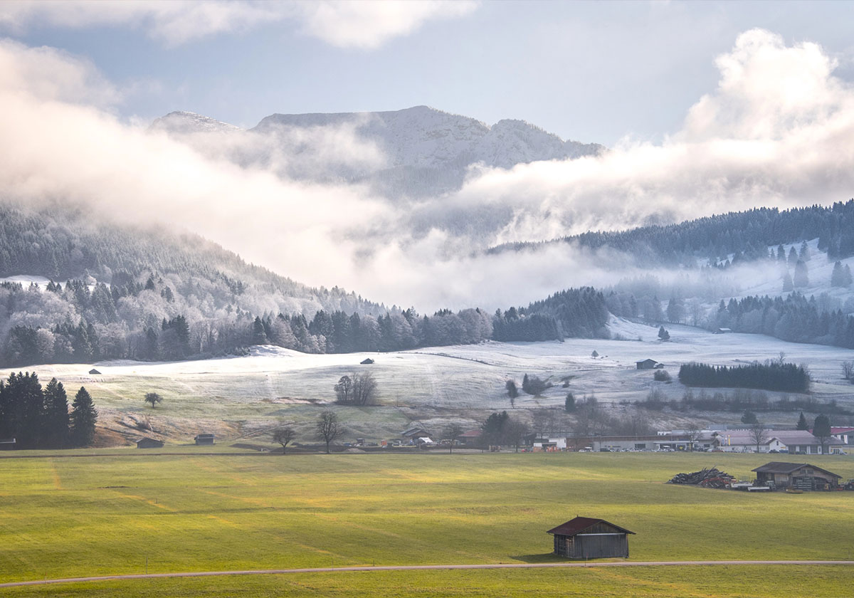 Frühlingslandschaft im Allgäu mit Nebel über Wiesen und Bergen